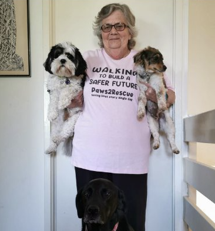 A photo of Paws2Rescue team member Gayleen smiling while standing in a pink t-shirt holding 2 small dogs